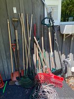 Group of assorted long-handled garden tools leaning against wall