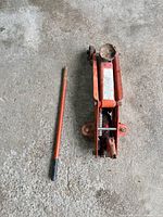 Top view of orange hydraulic floor jack and handle on concrete