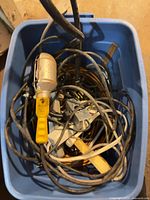 Top view of blue tote containing tangled extension cords, power strips, trouble light and assorted plugs