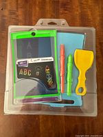 Front view of sealed Boogie Board LCD writing tablet kit showing tablet, stylus pens, scraper tool and stand