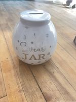 Front view of white ceramic swear jar coin bank showing gold text and symbols