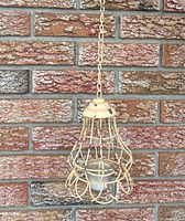 Full view of hanging metal candle holder with chain against brick wall