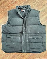 Front view of black puffer vest showing zipper, snap placket, flap pockets, collar, overall condition