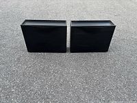 Front view of both black plastic wall-mount bins side by side on pavement