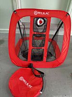 Front view of unfolded red/black Relilac target net with carry bag laid in front