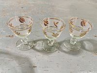 Three clear glass cordial glasses with gold trim and frosted band