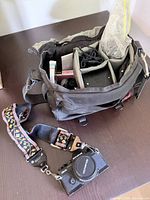 Camera body with mounted lens, strap, and open camera bag showing compartments