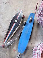 Wooden skateboard and blue Razor plastic cruiser board next to Razor scooter deck