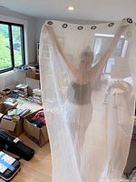 Person holding up one white sheer curtain panel showing full length and grommets