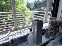 Group of vases on windowsill including rectangular block, grey ceramic, frosted bottle, jar with stones, hurricane vase with corks