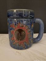 Mug with lid assembled, showing sun design and blue glaze