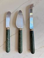 Three Sheffield stainless steel utensils with green marble handles on marble surface