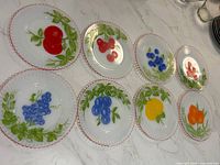 All eight 7-inch Petalware plates displayed, showing assorted fruit motifs and red-edged fluted rims