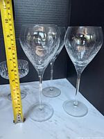 Tall stemmed wine glasses beside tape measure showing height