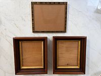 Three frames arranged on surface: two matching square frames with gilt liners and one striped rectangular frame