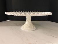 Side view of milk glass cake stand showing hobnail base and ruffled edge