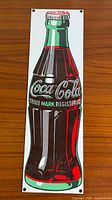 Full view of porcelain enamel Coca-Cola bottle sign on wood surface