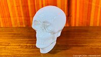 Front three-quarter view of white milk glass skull on wood surface