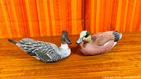 Both duck decoy sculptures side by side on wooden surface