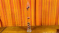 Full view of 21" glass Galileo thermometer on wood surface