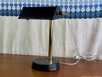Front view of banker style desk lamp showing black shade, brass stem, round base