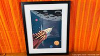 Full view of framed print displaying rocket and moon design