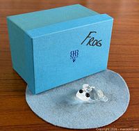 Frog figurine displayed on felt pad beside blue Swarovski box
