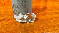 Crystal rhinoceros figurine beside cylindrical box for scale on wood surface