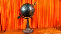 Full view of painted metal globe on pedestal stand
