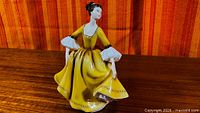 Full view of Royal Doulton Stephanie figurine in yellow dress on wood surface