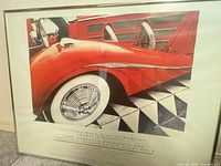 Full frontal view of framed poster showing image of red car, tire and frame