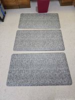 Three grey anti-fatigue mats laid out on floor with waste basket in background