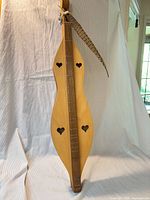 Full frontal view of wooden mountain dulcimer with heart sound holes and feather on headstock