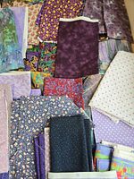 Assorted purple, blue and multicolour cotton fabric pieces laid out showing different prints and sizes