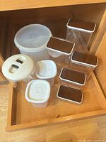 All ten plastic food storage containers inside cabinet showing shapes and lid colors