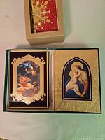 Open gift box showing two gold foil embossed religious greeting card designs inside.