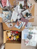 Overview of three boxes containing bagged miniatures, loose dollhouse furniture and craft supplies