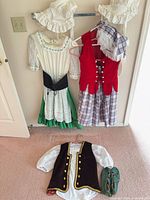 Full set on wall and floor showing dress, red vest/skirt, bonnets, brown vest/blouse and shoes