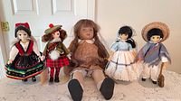 Group of five porcelain-head cloth-body dolls in assorted costumes on lace tablecloth
