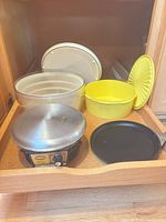 Drawer view showing crepe maker, crepe pan, yellow Tupperware bowl with lid, salad spinner parts