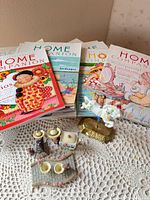 Stacked Mary Engelbreit Home Companion magazines and assortment of miniature figurines laid out on lace surface