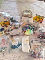 Overview of lot with boxed crayons, paint set, pastels, Ziploc bags of floss, tools and elastic