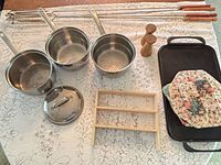Overall lot layout showing saucepans, griddle, skewers, rack, shakers and potholders