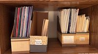 Four cardboard holders on shelf containing assorted craft pattern print materials