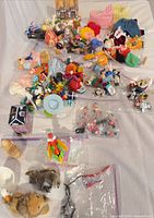 Overview of assorted toys, figurines, plush, doll clothes in multiple bags
