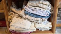 stacked folded linens on wooden shelf showing lace and solid pieces