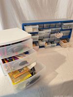 White Sterilite 3-drawer organizer open with art supplies visible; blue 24-drawer cabinet in background