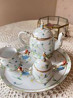 Full view of miniature porcelain tea set on tray showing floral pattern, gold trim, and small figural handles