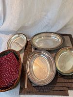 Four silver platters stacked with brown placemats underneath, wicker basket holding red cloth napkins