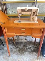 Singer Slant-O-Matic 401 machine mounted in two-drawer wood cabinet, tapered legs with brass caps, power pedal cord visible